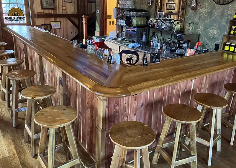 View of wooden bar made from light-colored wood and matching bar rail from Hardwoods Incorporated.