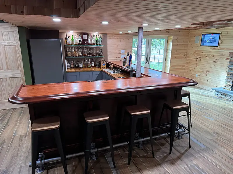 L-shaped bar made from dark colored wood with matching bar rail provided by Hardwoods Incorporated.